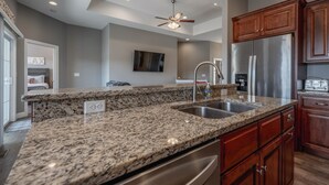 A kitchen with granite countertops, stainless steel appliances, wooden cabinets, and a ceiling fan.
