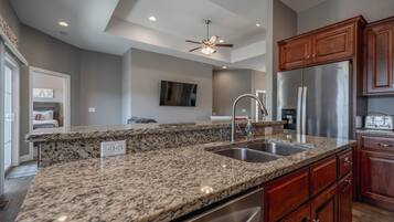 A kitchen with granite countertops, stainless steel appliances, wooden cabinets, and a ceiling fan.