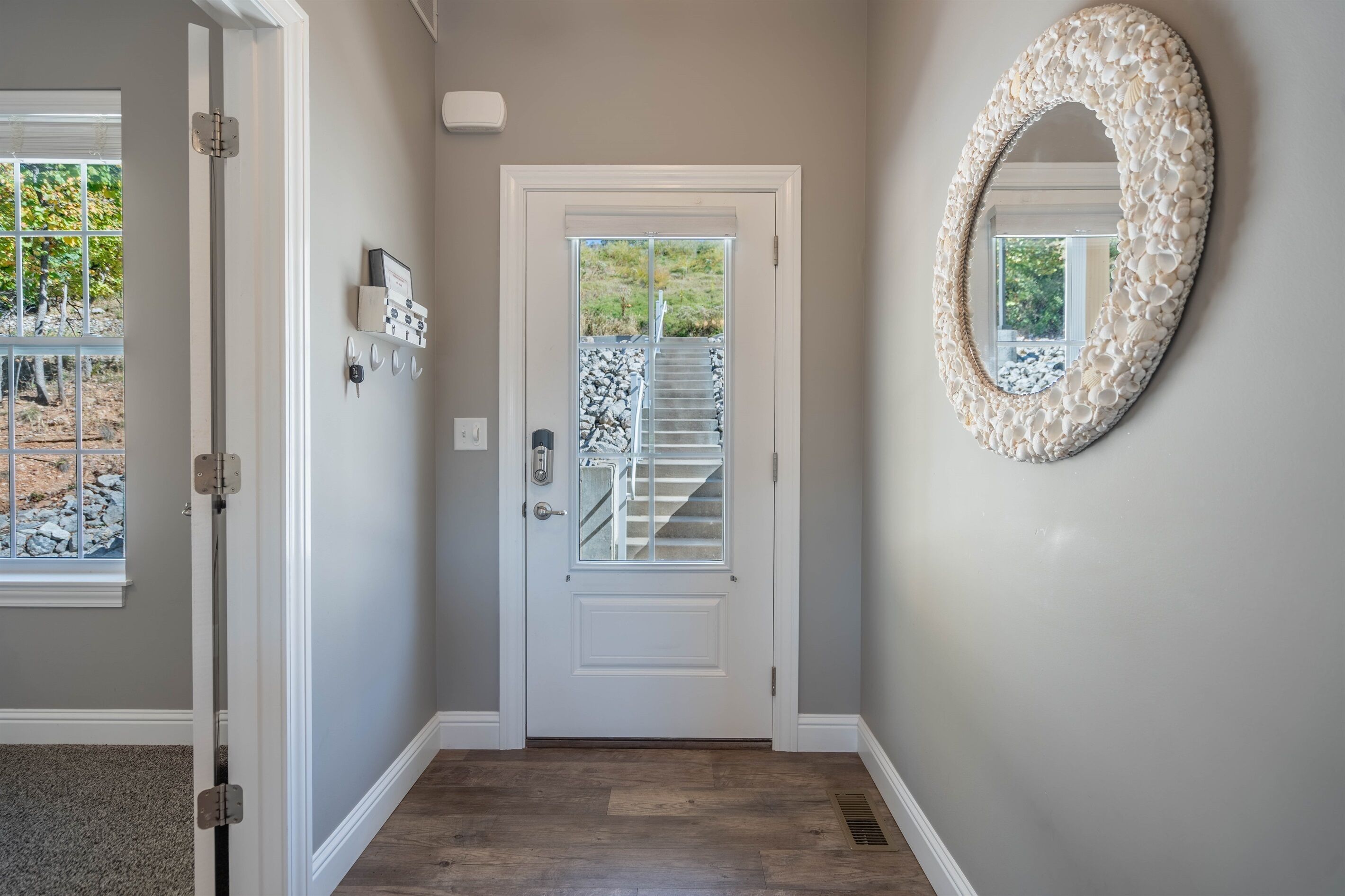 A hallway with a white door, a wall-mounted mirror, and a window with a view of a staircase and outdoor area.
