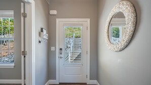 A hallway with a white door, a wall-mounted mirror, and a window with a view of a staircase and outdoor area.