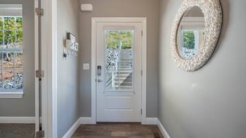 A hallway with a white door, a wall-mounted mirror, and a window with a view of a staircase and outdoor area.