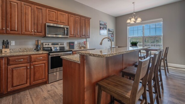 A modern kitchen with wooden cabinets, stainless steel appliances, a granite countertop, and a bar area with seating.