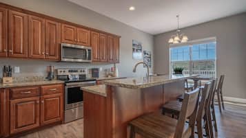 A modern kitchen with wooden cabinets, stainless steel appliances, a granite countertop, and a bar area with seating.