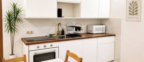 A compact kitchen with white cabinets, a microwave, a sink, and a stove. There is a potted plant and a framed picture on the wall.
