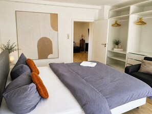 A modern bedroom with a large bed, a wardrobe, and a hallway leading to another room. - 1OG R City Wohnung Balkon nähe Salzburg (Freilassing)
