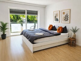 Un dormitorio moderno con una cama grande, una planta en maceta y vistas de vegetación por la ventana.