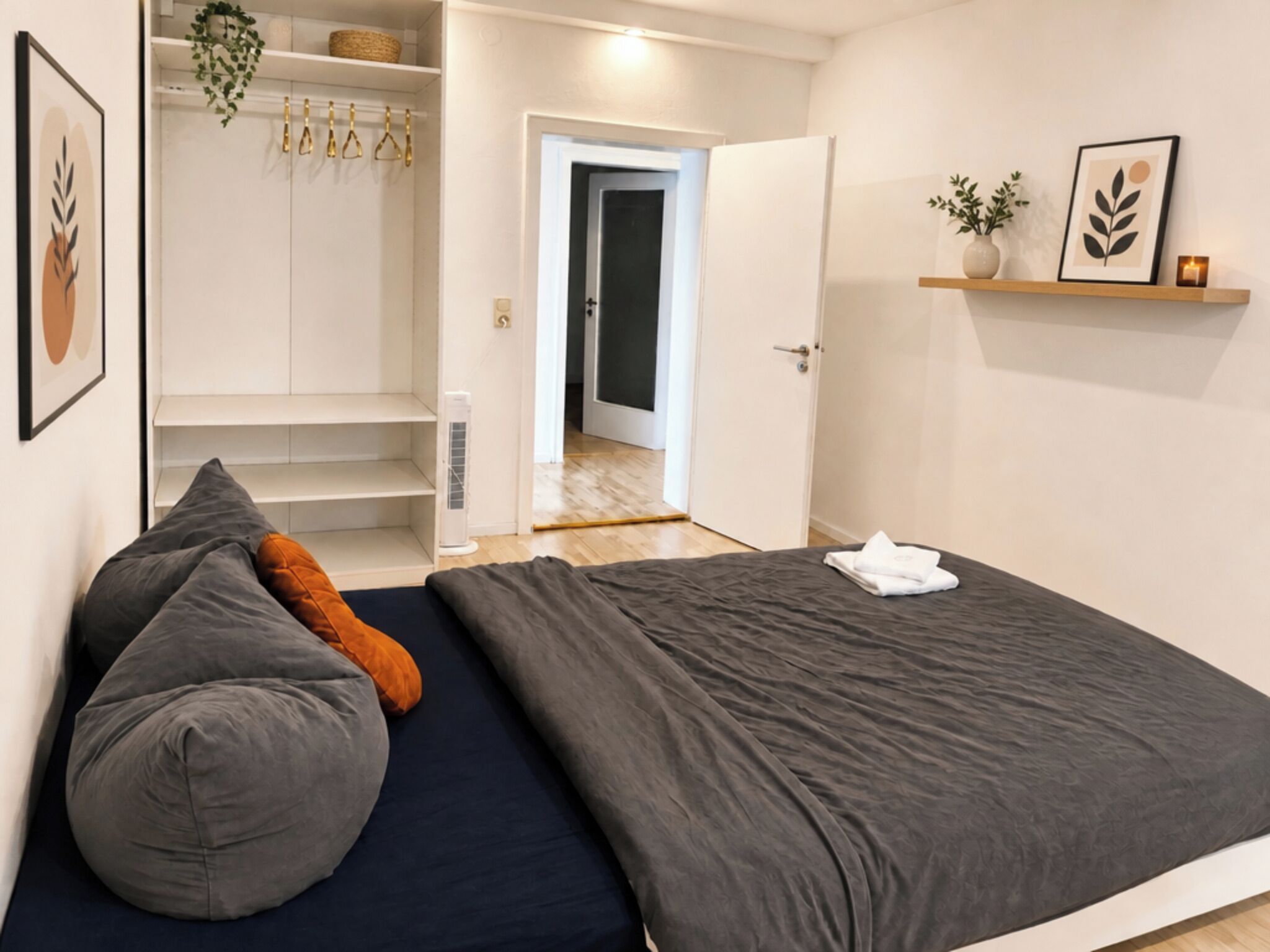 Une chambre à coucher comprenant un lit, des oreillers, une armoire, une porte donnant sur une autre pièce et une étagère avec des objets décoratifs.
