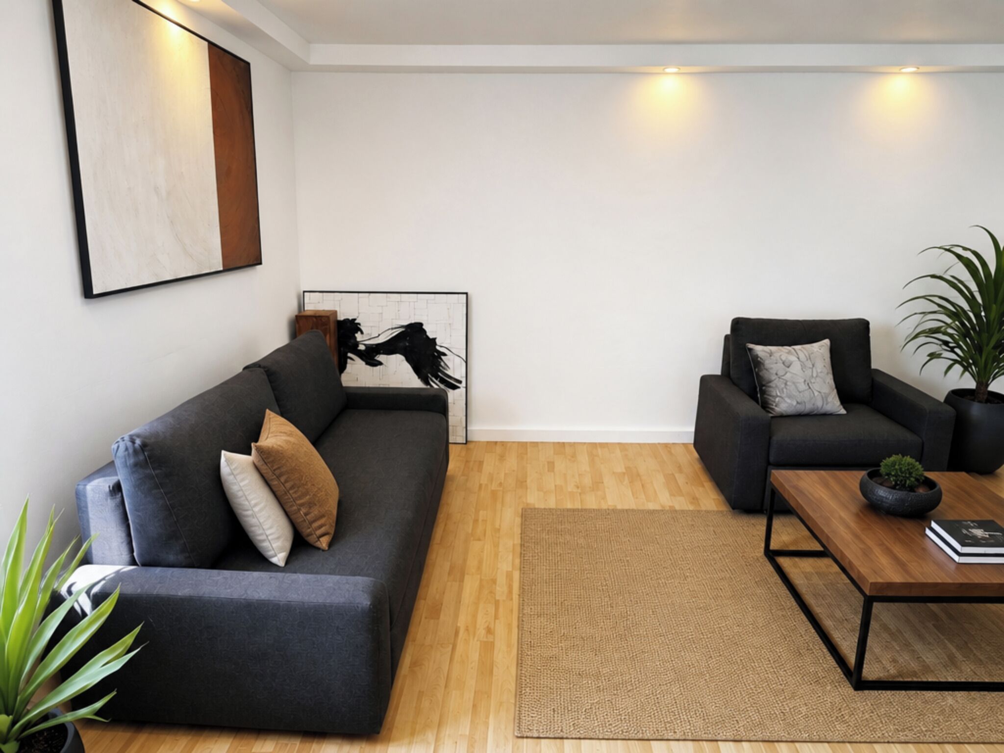 A modern living room with a dark grey sofa, a smaller armchair, a coffee table, and a framed artwork on the wall.