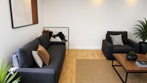 A modern living room with a dark grey sofa, a smaller armchair, a coffee table, and a framed artwork on the wall. - 1OG R City Wohnung Balkon nähe Salzburg (Freilassing)