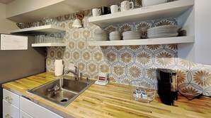 A modern kitchen with a stainless steel sink, wooden countertop, and built-in shelves holding serving dishes and coffee cups. - Casa Cielo (Santa Fe)