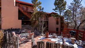 A wooden deck with outdoor seating, a stone fire pit, and a red railing. - Casa Cielo (Santa Fe)