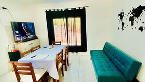 Un coin repas avec une table dressée pour quatre personnes, un téléviseur fixé au mur et un canapé de couleur turquoise.