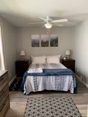 Ein Schlafzimmer mit einem Bett, zwei Nachttischen, einem Deckenventilator und einem Teppich.