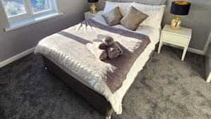 A neatly made bed with a beige comforter and pillows, a pair of rolled towels, and two bedside tables with lamps. - West Midlands Home - 3BR w/FREE Parking and WIFI (West Midlands)