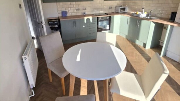 A compact kitchen with a round dining table, two chairs, and light green cabinets. - West Midlands Home - 3BR w/FREE Parking and WIFI (West Midlands)