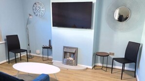 A living room with a fireplace, a flat-screen TV, and a round mirror on the wall. - West Midlands Home - 3BR w/FREE Parking and WIFI (West Midlands)