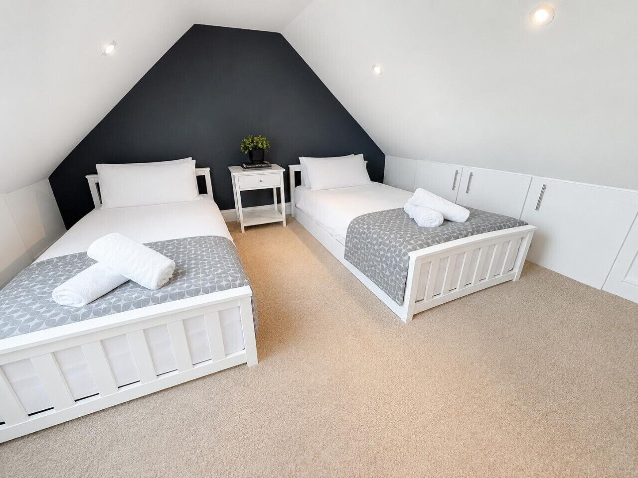 Ein Schlafzimmer mit zwei Betten, einem kleinen Nachttisch mit Pflanze und einem weißen Kleiderschrank.