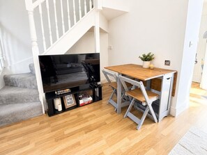 A room with a wooden floor, a white staircase, a black entertainment unit, and a wooden table with chairs. - 3BR Thames Retreat | Heathrow 10min | Train 5min (Egham)
