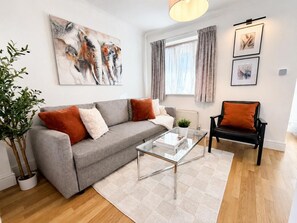 A modern living room with a grey sofa, a black armchair, a glass coffee table, and a potted plant. - 3BR Thames Retreat | Heathrow 10min | Train 5min (Egham)