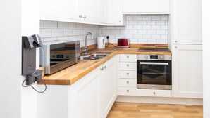 Moderni keittiö, jossa on valkoiset kaapit, puinen työtaso, sisäänrakennettu uuni ja kahvinkeitin.