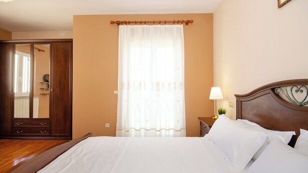Ein Hotelzimmer mit einem Bett, einem Holzschrank, einem fenster mit Vorhängen und einer Nachttischlampe.
