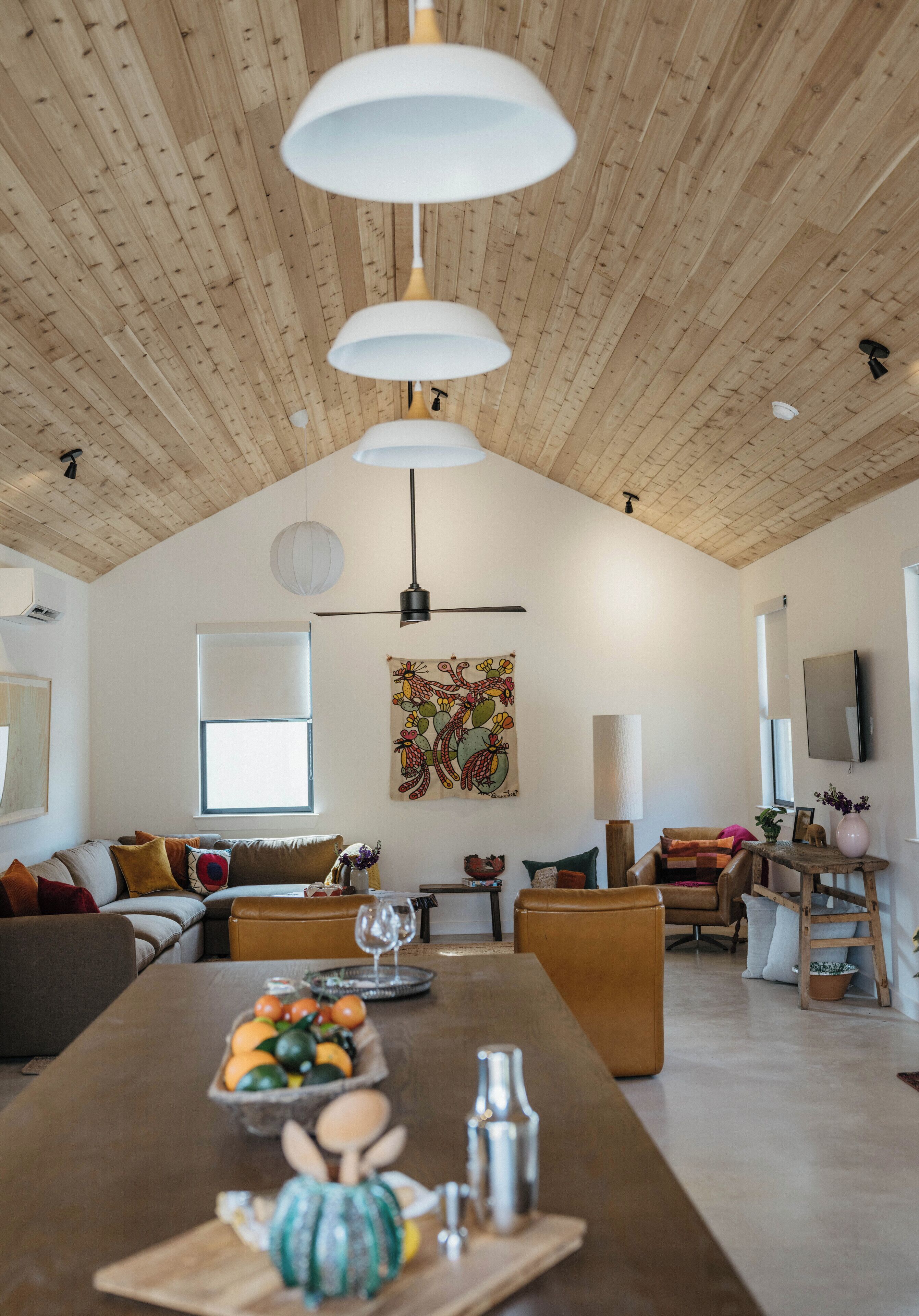 Un soggiorno spazioso con soffitto in legno, un'ampia finestra, un divano, un tavolino da caffè con della frutta e un quadro appeso al muro.