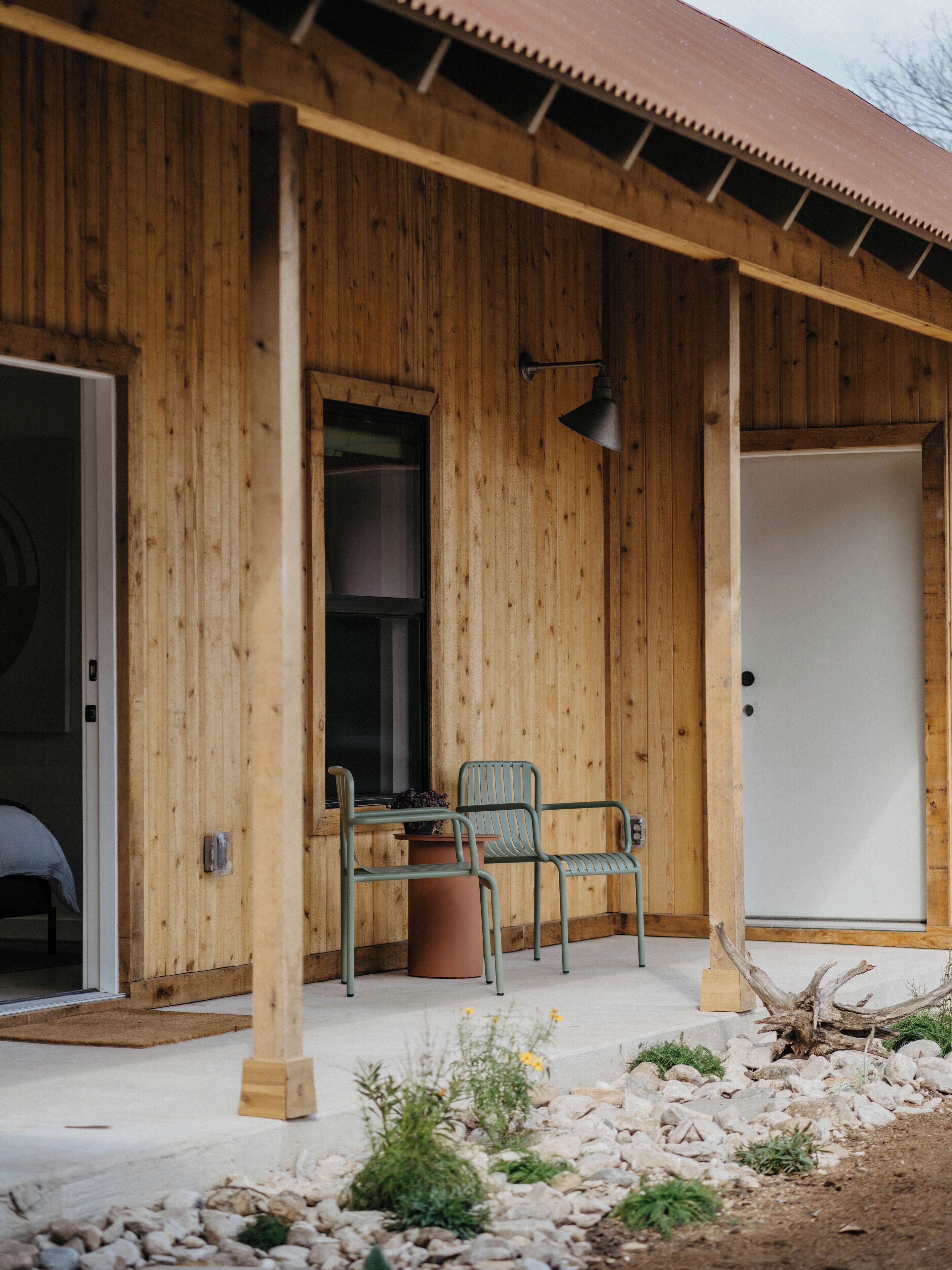 A wooden building with a covered porch, two chairs, a table, and a door.