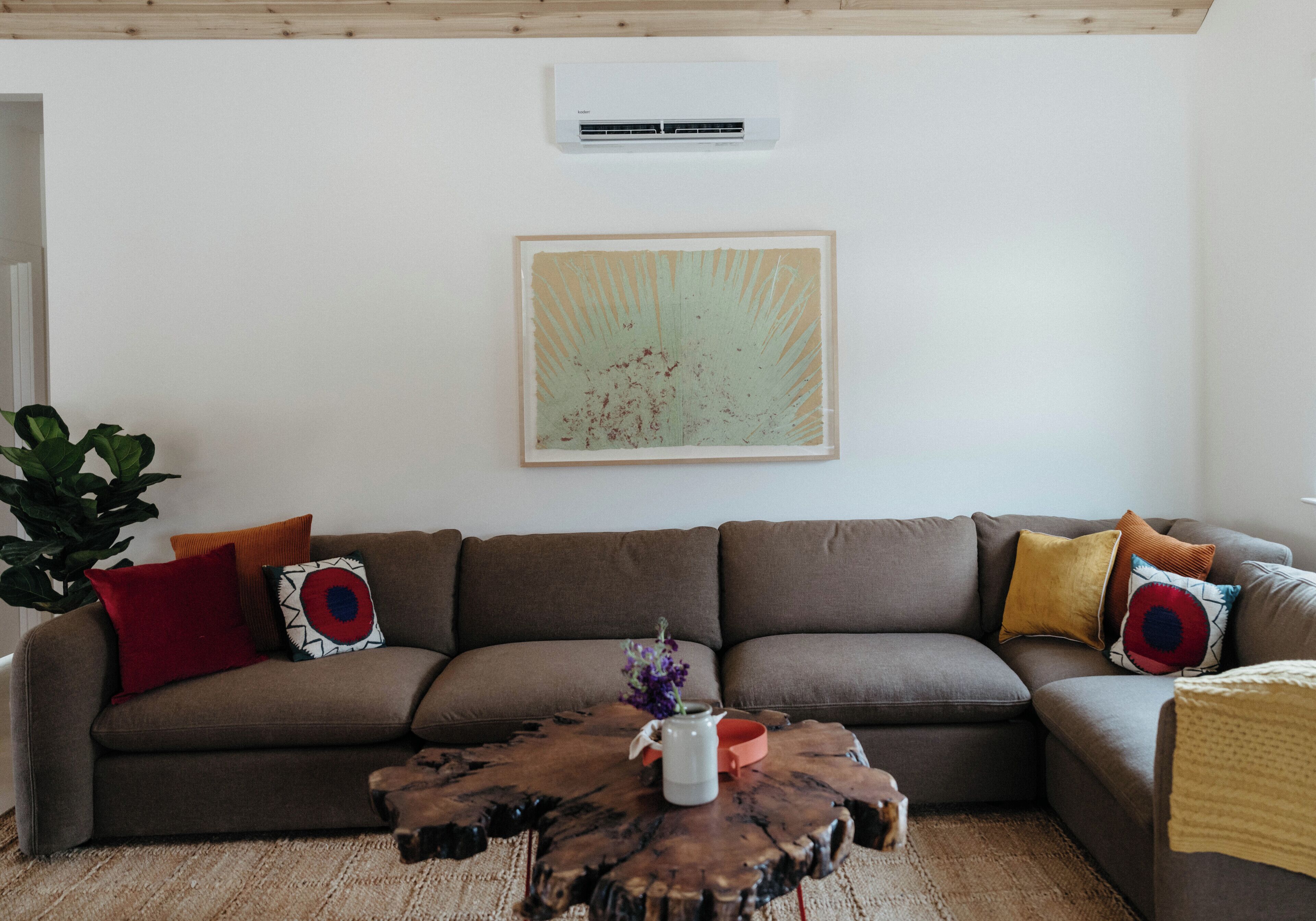 A living room with a brown sectional sofa, a wooden coffee table, and a large abstract painting on the wall.