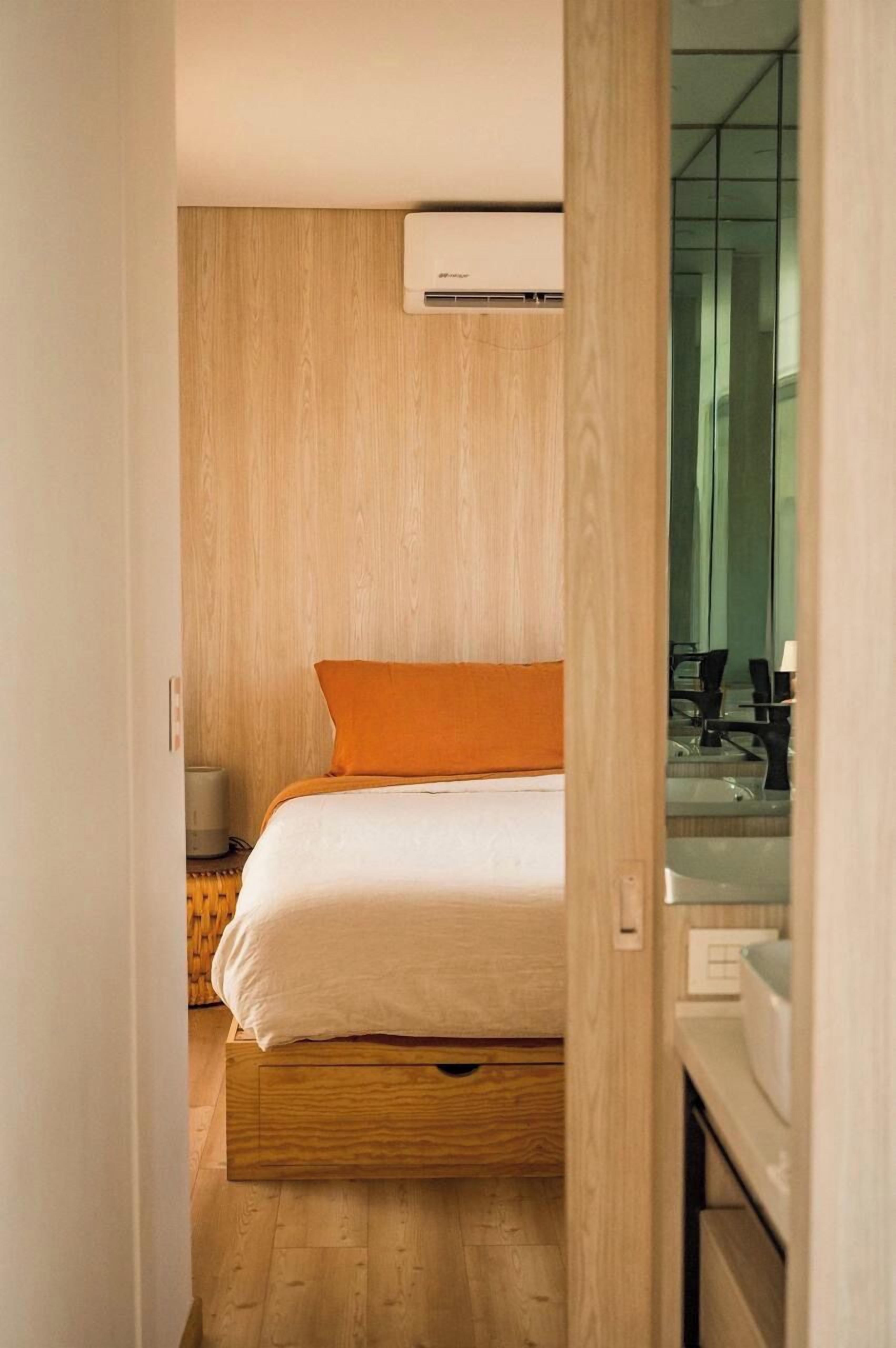A bedroom with a bed, an air conditioner, a wooden floor, and a mirror.