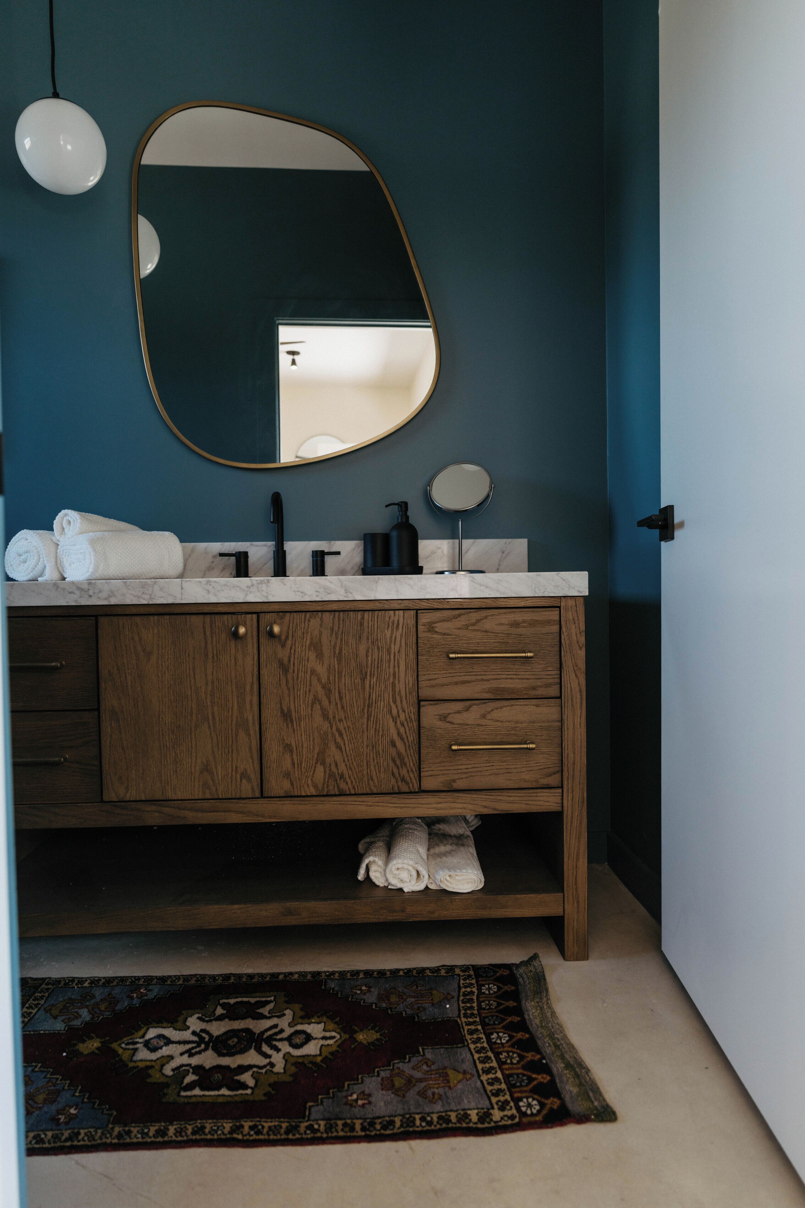 Une salle de bain avec un meuble-lavabo en bois, un grand miroir et un plan de toilette en marbre.