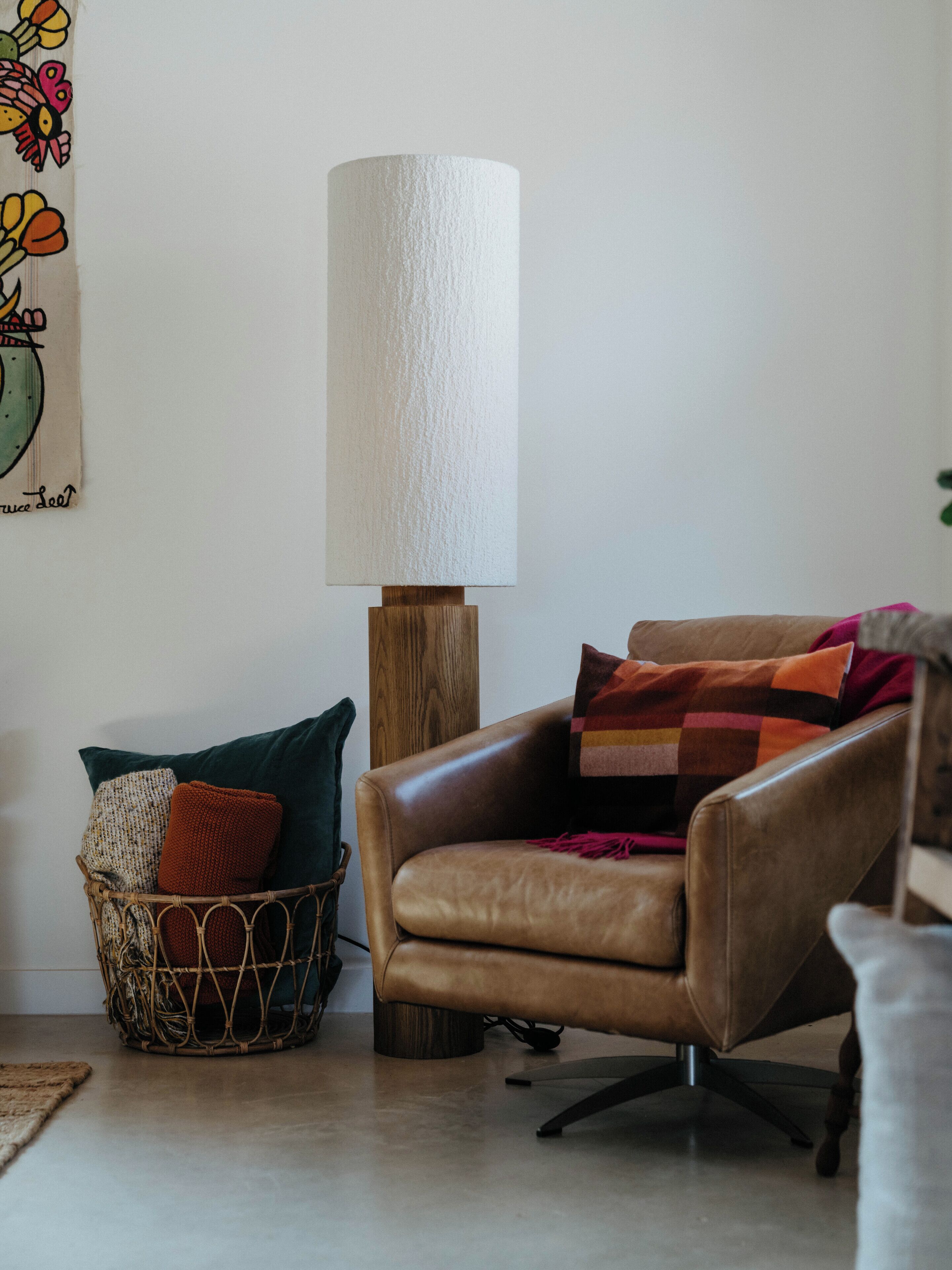 A leather armchair with a cushion, a floor lamp, and a woven basket with pillows.