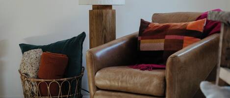 A leather armchair with a cushion, a floor lamp, and a woven basket with pillows.