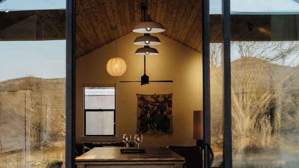 A modern interior with a wooden ceiling, a dining area with a table and chairs, and a large window offering a view of the outdoors.