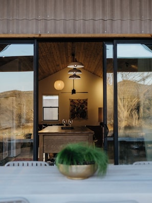 A modern interior with a wooden ceiling, a dining area with a table and chairs, and a large window offering a view of the outdoors. - Camp Cold Springs (Concan)
