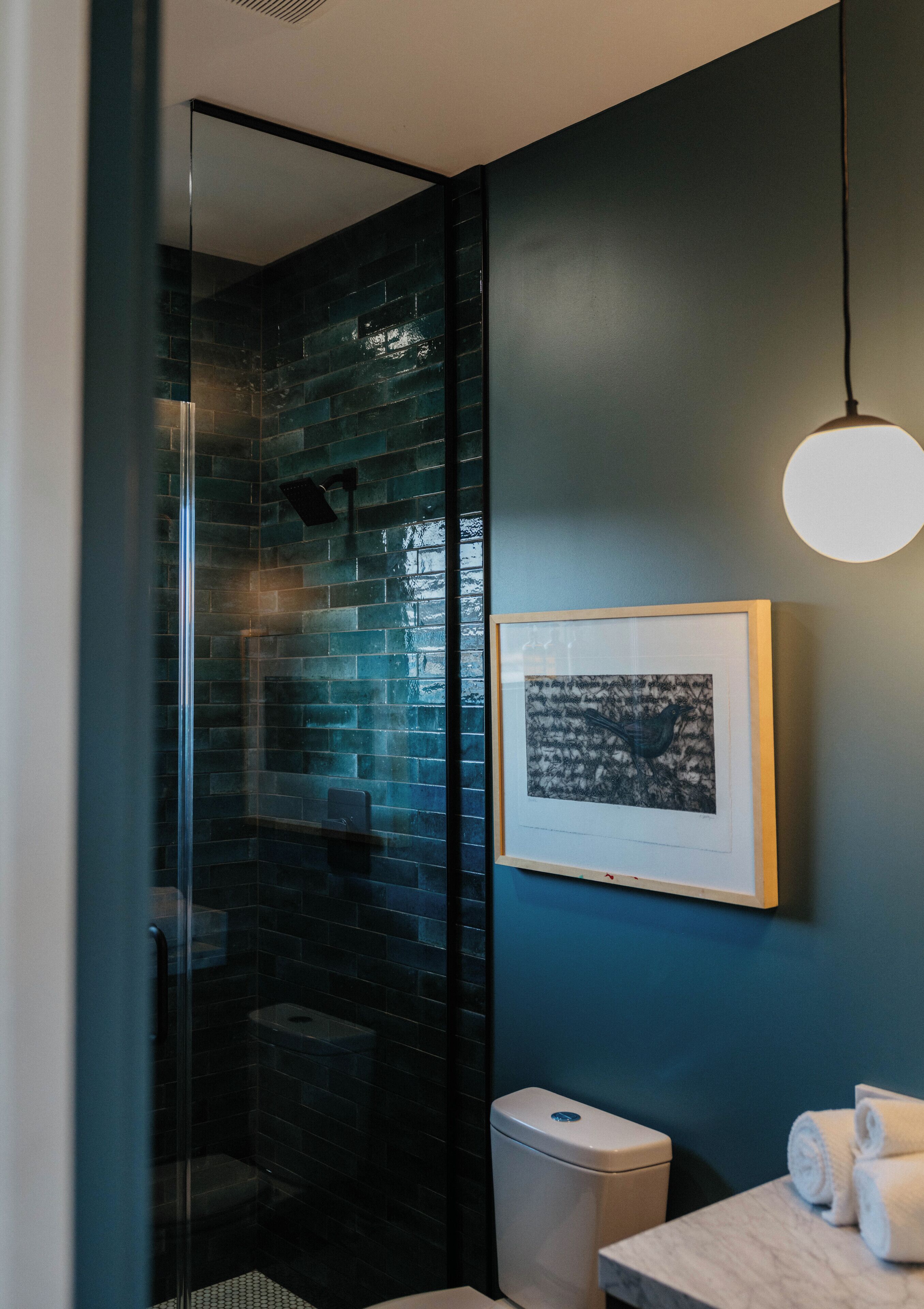 Une salle de bain moderne avec une douche à parois de verre, une œuvre d’art encadrée au mur et des toilettes blanches.