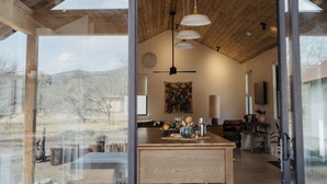 A spacious living area with a wooden ceiling, a large window offering a view of the outdoors, and a central table with decorative items.