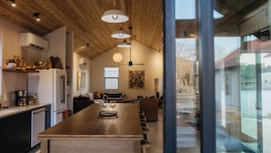 A modern kitchen with a wooden ceiling, a central island, and a large window overlooking a snowy landscape.
