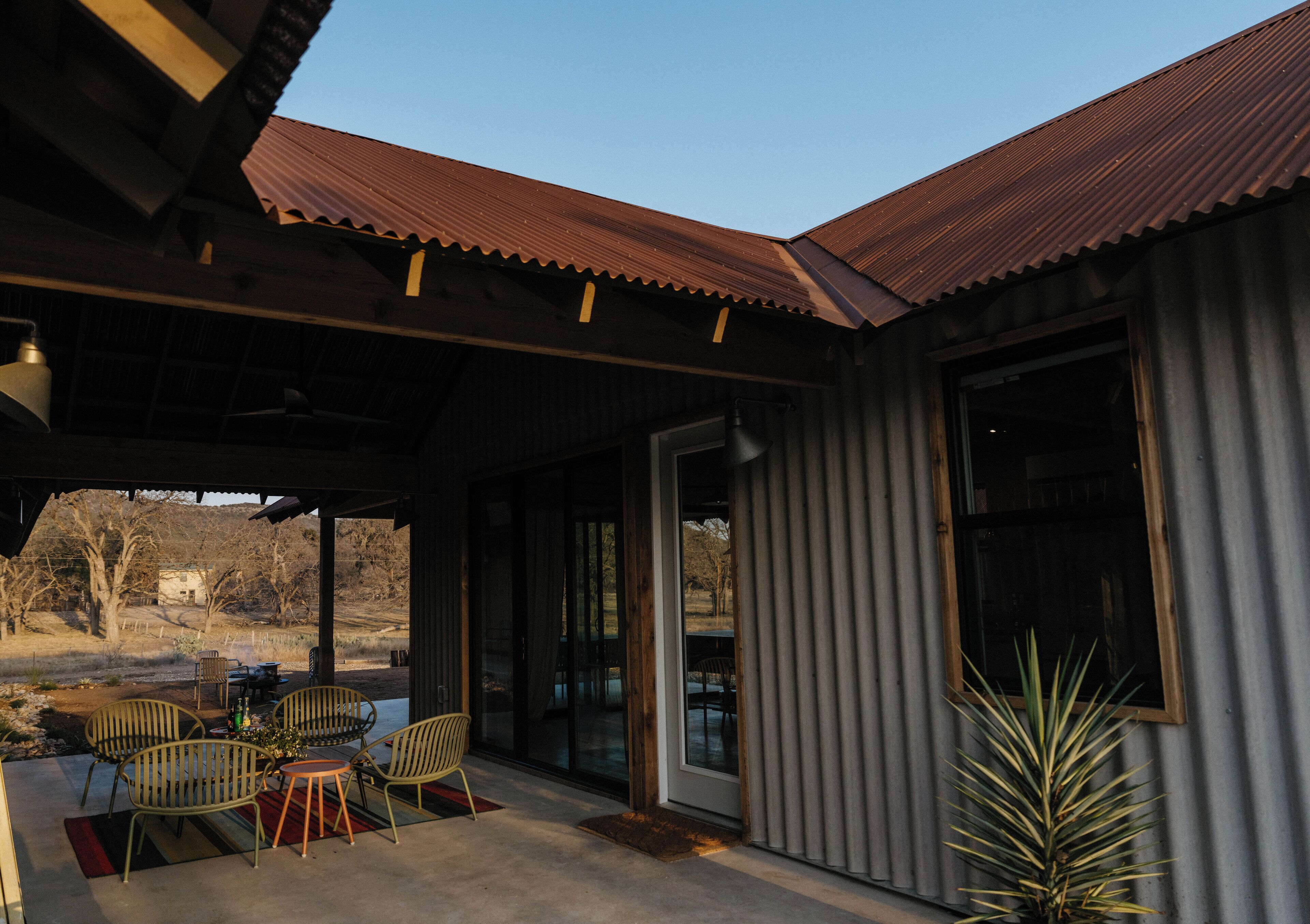 An outdoor patio with a covered seating area, a sliding glass door, and a view of the surrounding landscape.