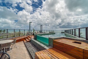 A rooftop infinity pool with wooden deck seating and a glass balustrade overlooking the ocean. - Comfort in Beachfront Condo W/pool Bre0116 (João Pessoa)