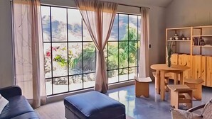 A modern living room with a large window, a sofa, an ottoman, a wooden dining table, and a chair. - Loft Casa ODA, beautiful mountainfront retreat, quiet luxury (Amatlán de Quetzalcóatl)