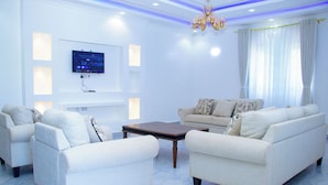Een moderne woonkamer met een flatscreen televisie aan de muur, een kroonluchter en een zithoek.