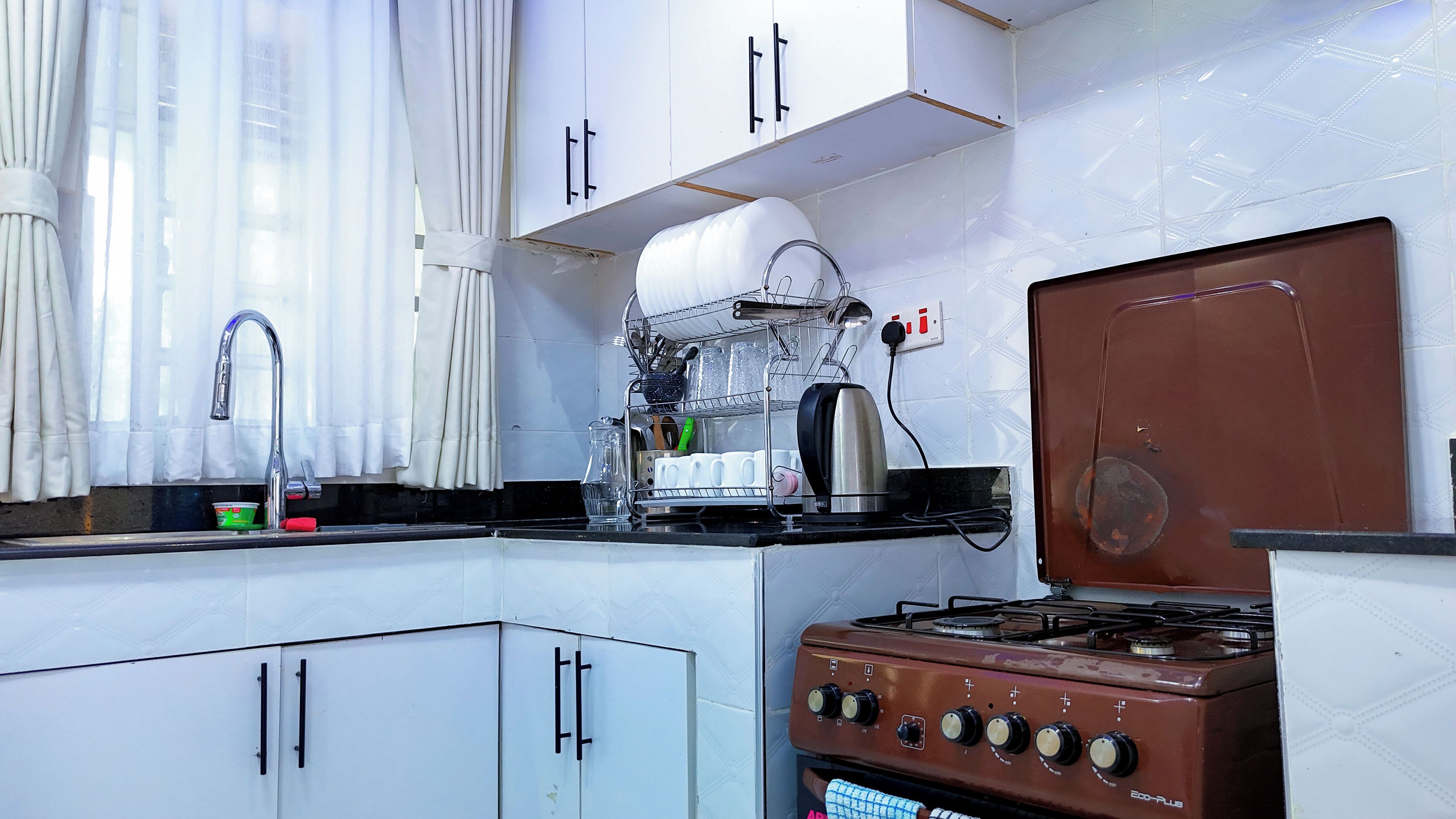 A kitchen with white cabinets, a stainless steel sink, a dish rack, and a brown gas stove.
