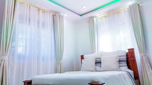 Een slaapkamer met een bed, gordijnen en een plafondlamp.