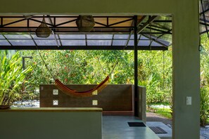 A covered outdoor area with a hammock, potted plants, and a view of a lush garden. - Casa Jocote: Rainforest Dream House in Cabo Matapalo (puerto jimenez)