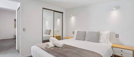 A modern hotel room with a large bed, a bedside table, a nightstand, and a mirror.