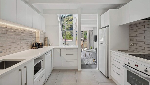Una cucina moderna con mobili bianchi, forno integrato e un'ampia finestra con vista su un giardino.