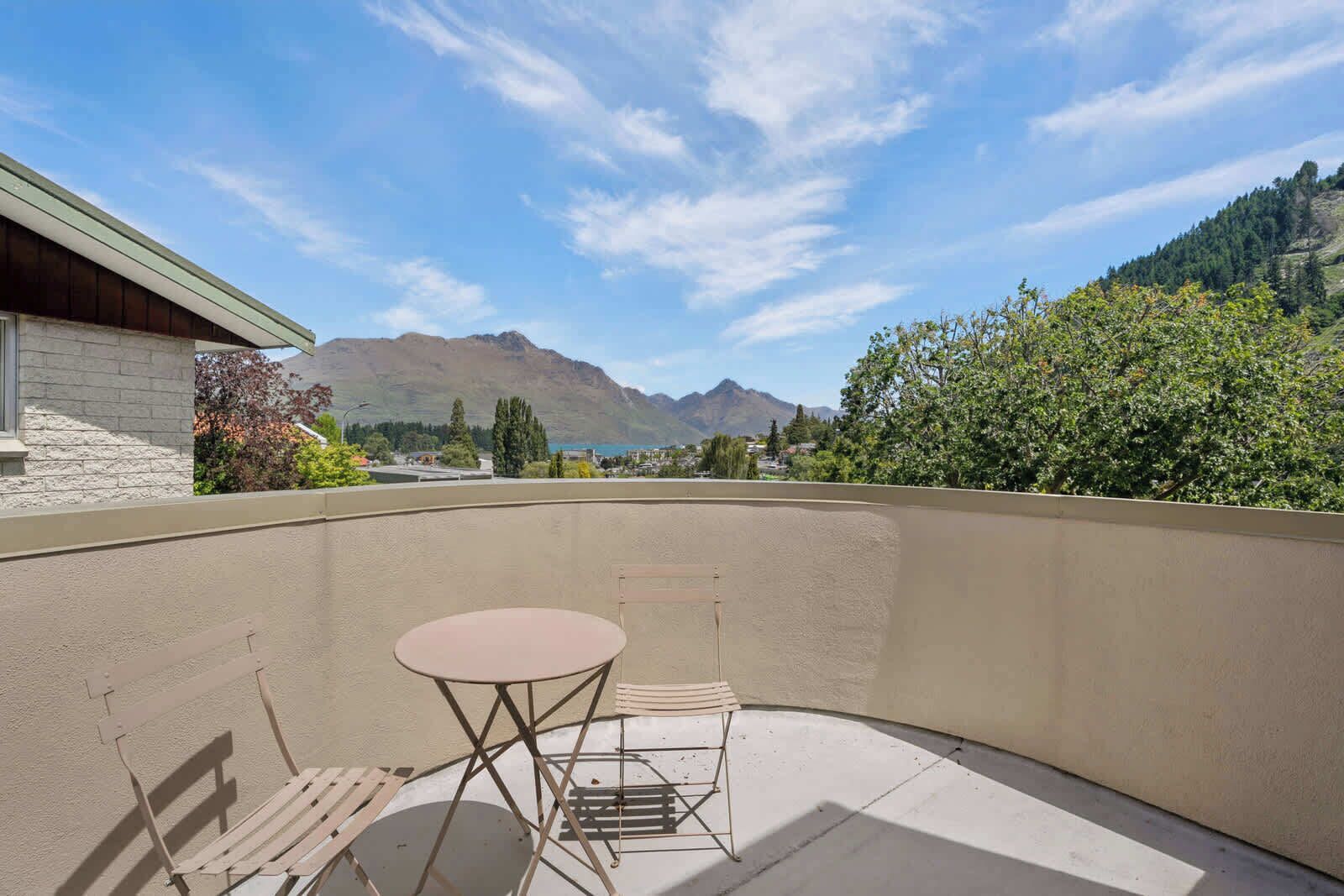 A balcony with a table and chairs, overlooking a mountainous landscape.