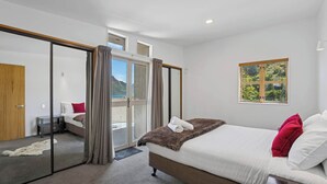 A modern bedroom with a large bed, a sliding glass door leading to a balcony, and a view of greenery. - Peaks & Cranbury 17B:  Location & Views ! (Queenstown)
