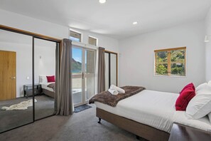 A modern bedroom with a large bed, a sliding glass door leading to a balcony, and a view of greenery. - Peaks & Cranbury 17B:  Location & Views ! (Queenstown)