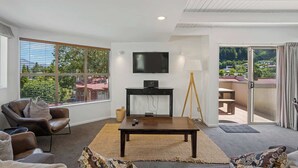 A modern living room with a large window, a flat-screen TV, a wooden coffee table, and a sofa. - Peaks & Cranbury 17B:  Location & Views ! (Queenstown)